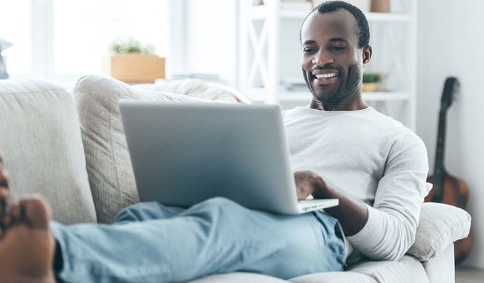 african american man relaxed and happy at home on couch with laptop