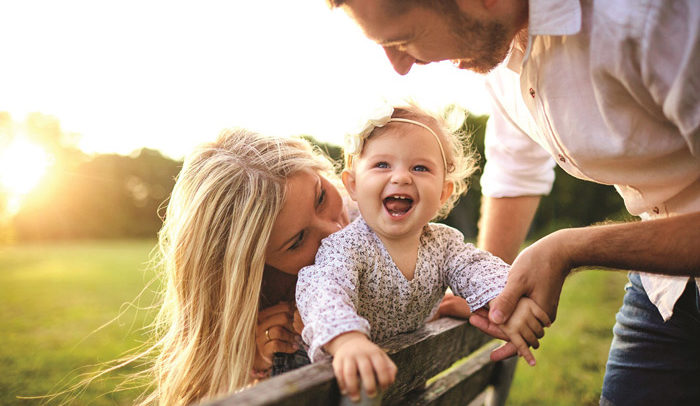 family outside in sunshine on a park bench with smiling baby